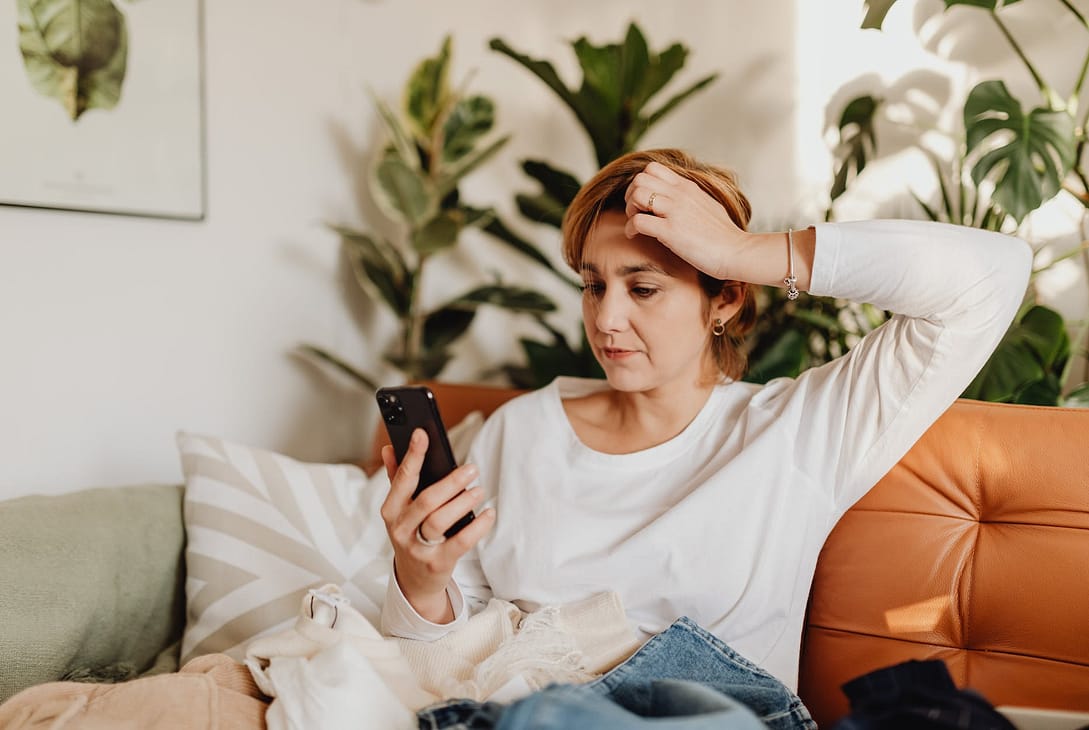 woman sitting on sofa looking at phone and scratching her head