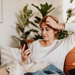 woman sitting on sofa looking at phone and scratching her head