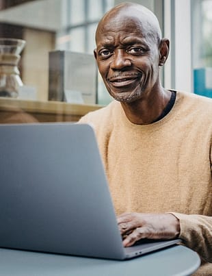 smiling middle aged black man working remotely on netbook in cafe